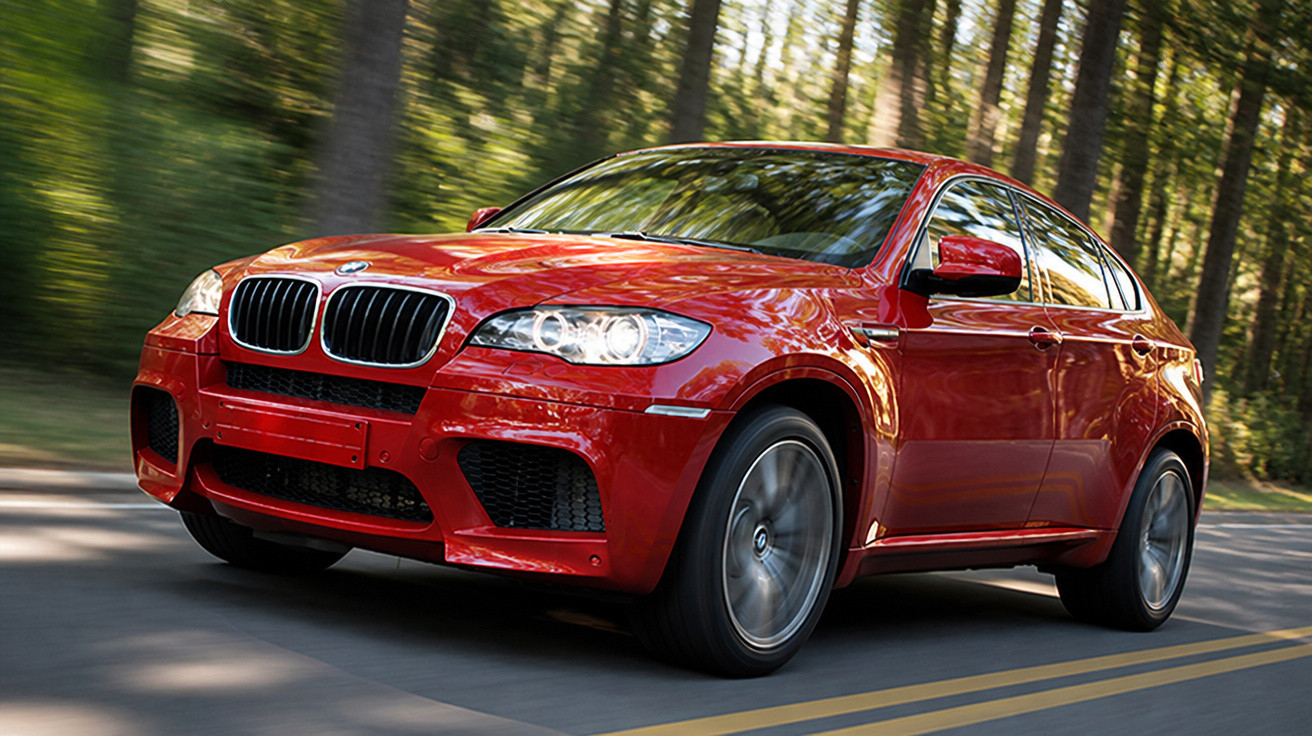 Carro vermelho BMW a alta velocidade numa estrada rodeada de árvores.