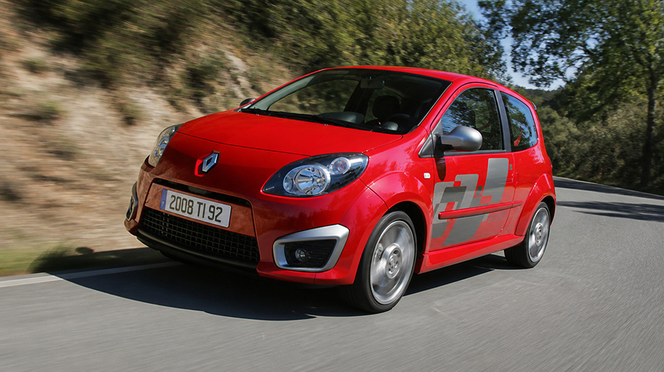 Carro compacto vermelho Renault a circular numa estrada curva com árvores e vegetação ao lado.
