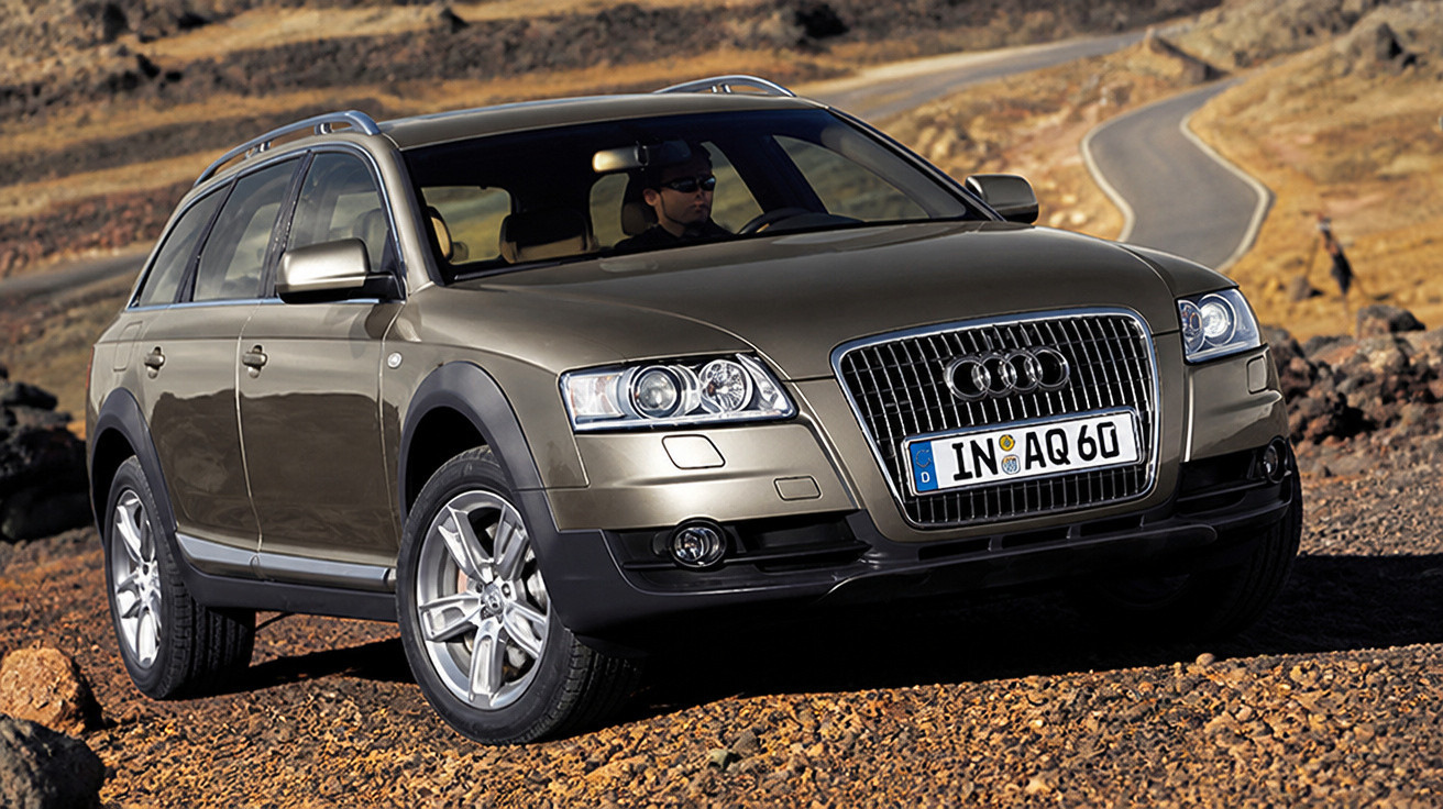Carro Audi Allroad cinzento estacionado em terreno rochoso com homem ao volante.
