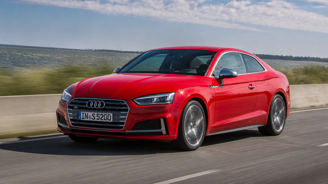 Audi desportivo vermelho a circular numa estrada junto a um lago num dia de céu parcialmente nublado.